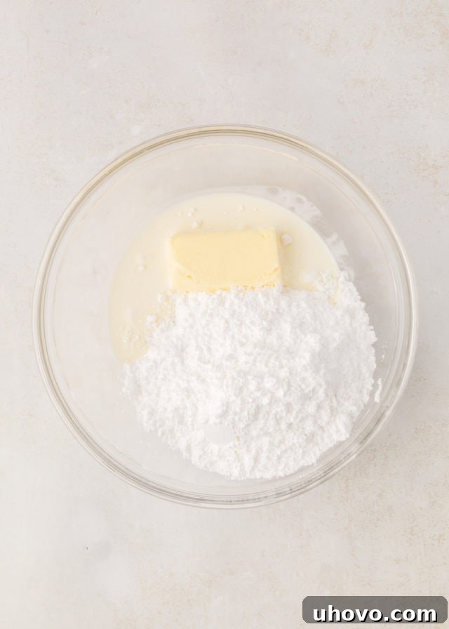 Overhead view of confectioners' sugar, softened butter, heavy cream, and peppermint extract in a mixing bowl, ready to be combined for frosting.