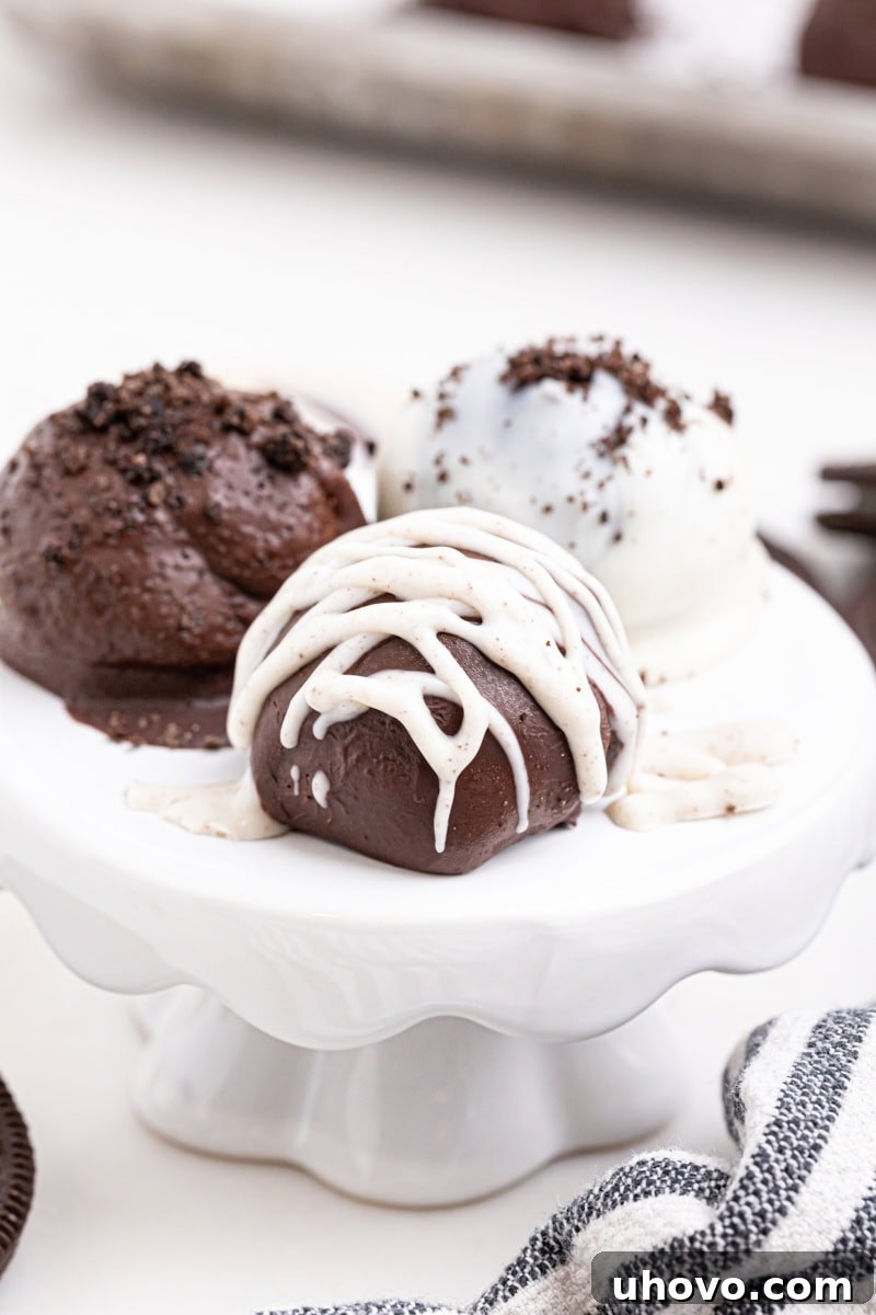 Three perfectly formed Oreo truffles, one with white chocolate drizzle, presented elegantly on a small white pedestal.