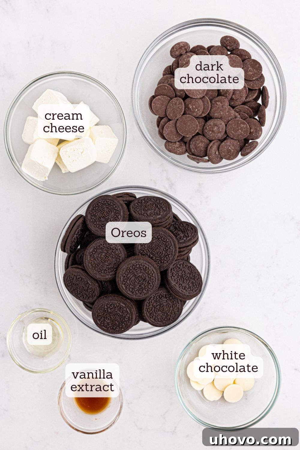 Overhead view of ingredients for Oreo truffles laid out on a surface, including a package of Oreos, a block of cream cheese, vanilla extract, and chocolate melting wafers.