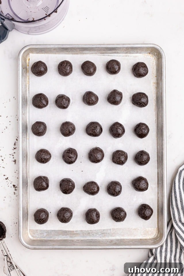 Overhead view of Oreo truffle mixture formed into small, uniform balls and arranged on a parchment-lined baking sheet.