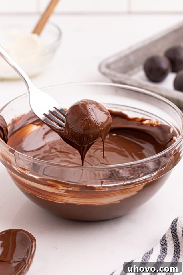 A single Oreo truffle being carefully dipped into a bowl of melted dark chocolate using a fork.