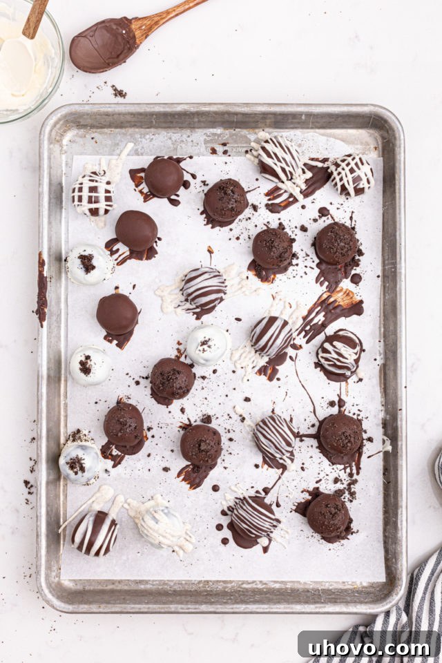Overhead view of freshly dipped Oreo truffles, some with sprinkles, arranged on a parchment-lined baking sheet to set.