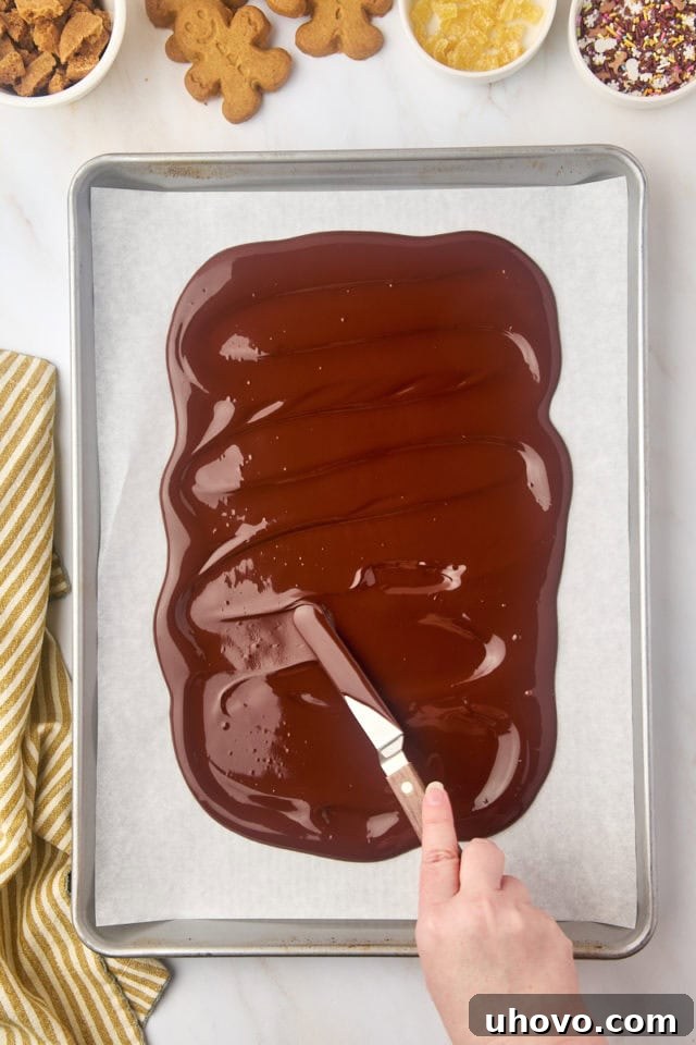 overhead view of melted chocolate being spread in a thin layer on a parchment-lined baking sheet