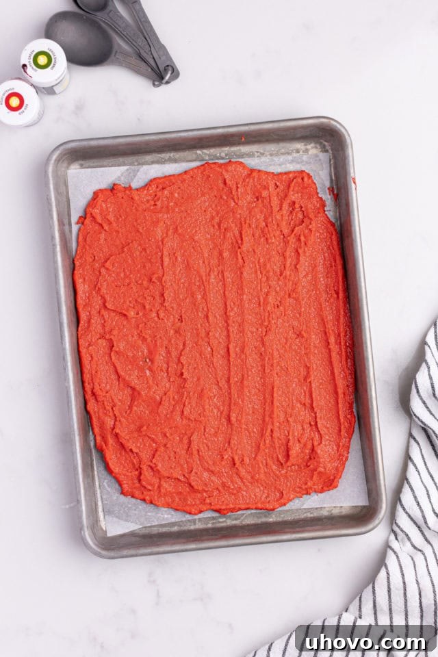 Overhead view of red cookie dough spread evenly in a parchment-lined baking pan.