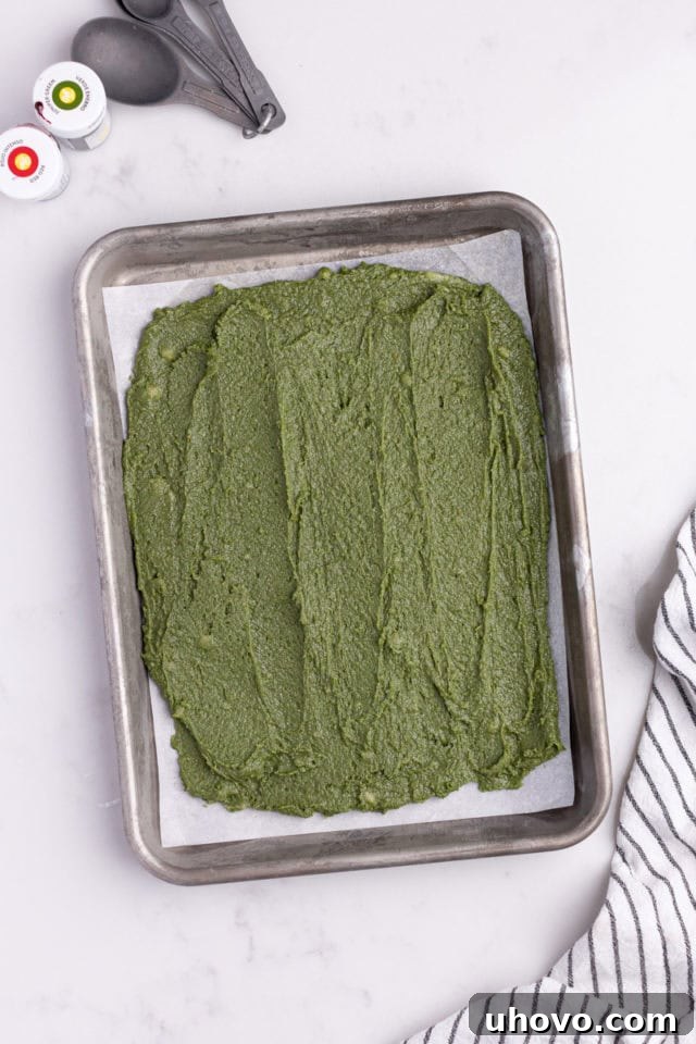 Overhead view of green dough spread evenly in a parchment-lined baking pan.