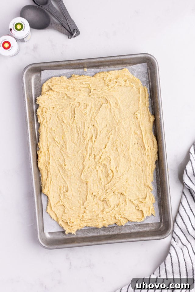 Overhead view of untinted Italian rainbow cookie dough spread evenly in a parchment-lined baking pan.