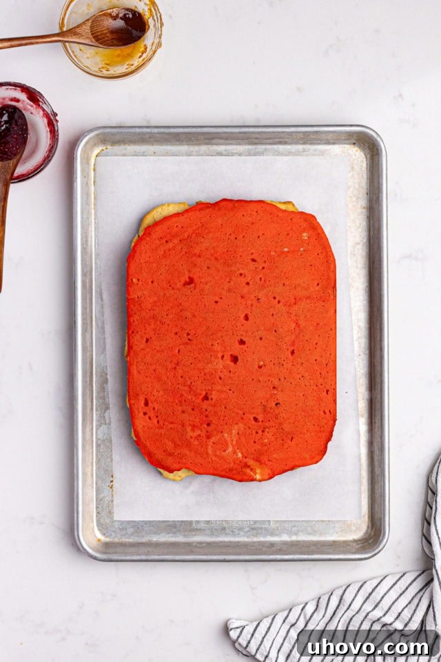 Overhead view of the red layer of Italian rainbow cookies being carefully placed on top of the other layered components.