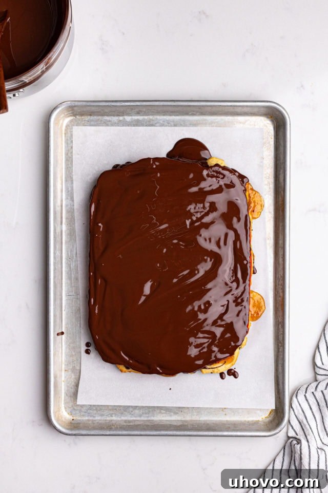 Overhead view of melted dark chocolate being spread smoothly over the top of the red layer of Italian rainbow cookies, allowed to set.