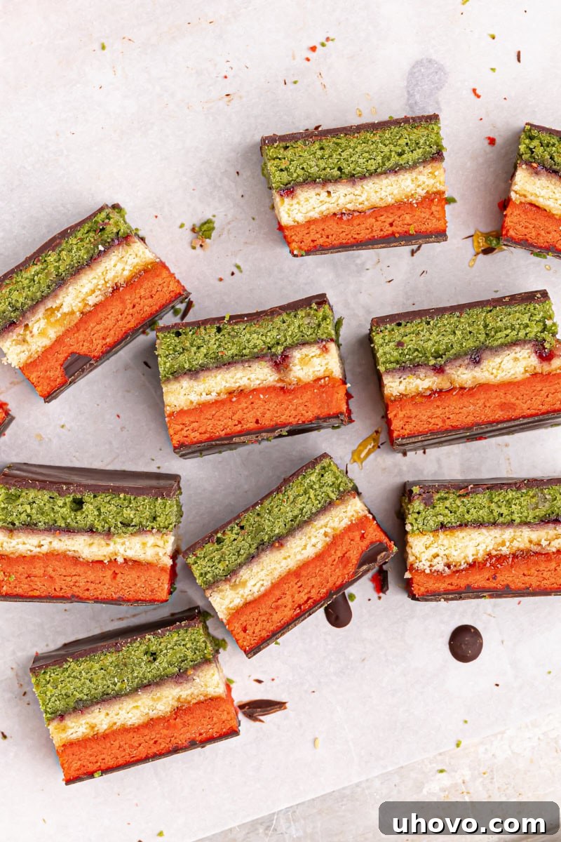 Overhead view of Italian rainbow cookies arranged on their sides on parchment paper, showing the beautiful layers and chocolate.