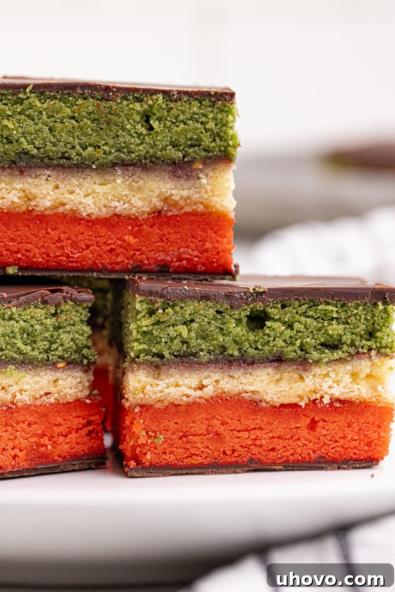 Close-up of three Italian rainbow cookies on a white plate, highlighting their vibrant colors and chocolate coating.