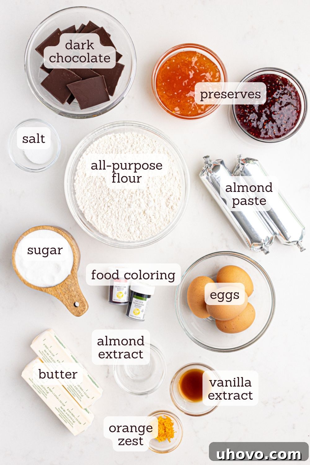 Overhead view of various ingredients laid out for making Italian rainbow cookies, including flour, sugar, butter, eggs, preserves, and chocolate.