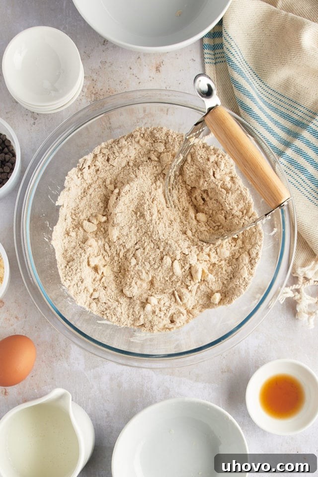 Overhead view of a pastry blender being used to cut cold butter into the dry scone ingredients, creating a coarse meal texture.