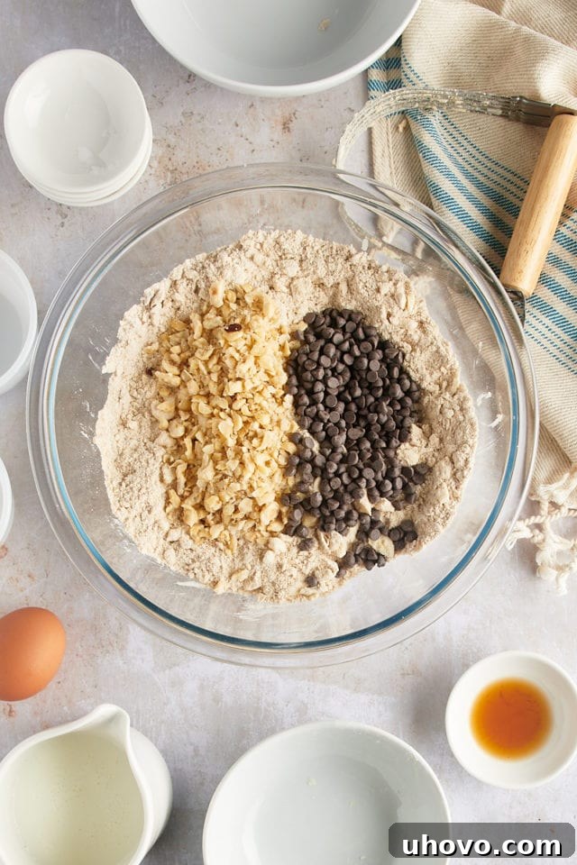 Overhead view of toasted hazelnuts and mini chocolate chips being added to the dry scone mixture in a mixing bowl.