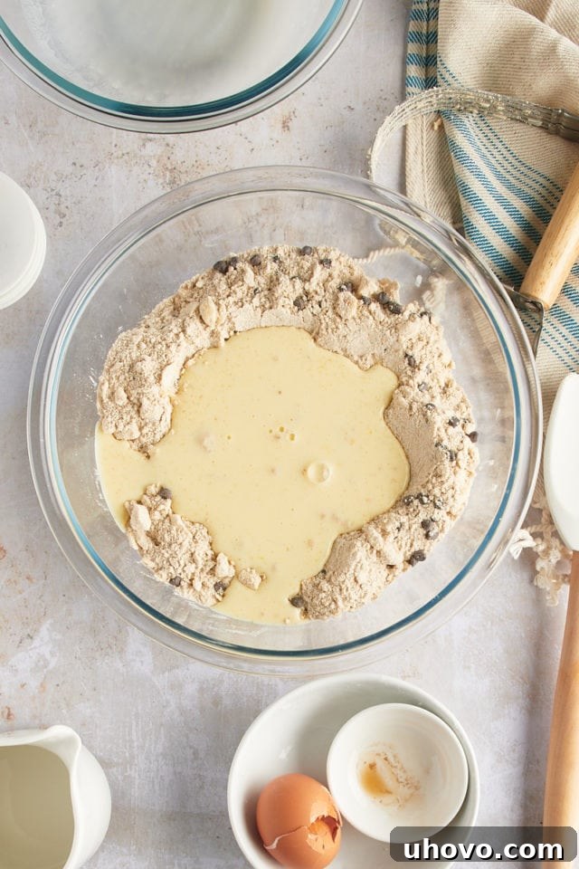 Overhead view of liquid ingredients (buttermilk, egg yolk, vanilla) being poured into the bowl of dry scone ingredients.