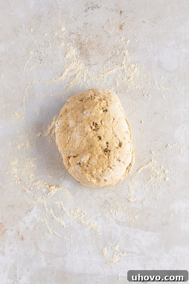 Overhead view of scone dough being gently kneaded on a floured surface, ready for shaping.