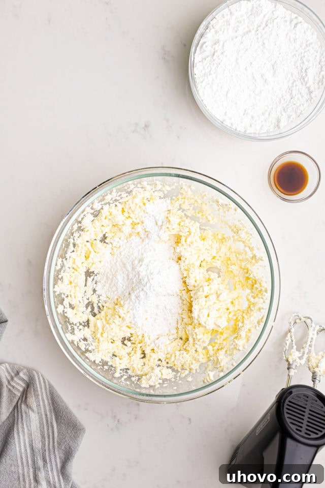 Confectioners' sugar being gradually added to the creamed butter and cream cheese in a mixing bowl, showing the frosting mixing process.