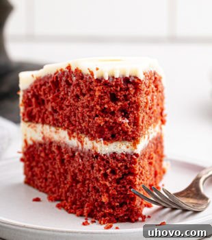 A slice of red velvet cake on a white plate with a bite missing