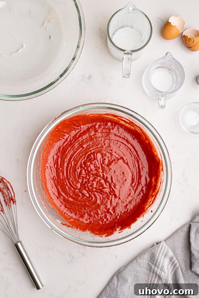 A close-up overhead view of the rich, deep red red velvet cake batter in a mixing bowl, perfectly smooth and ready for baking.