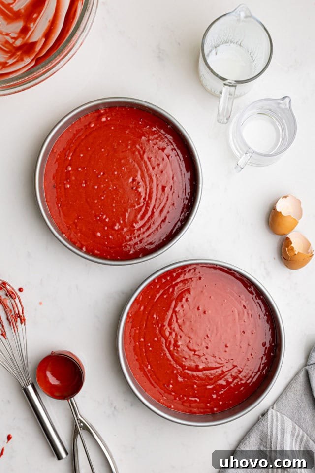 The vibrant red velvet cake batter evenly divided between two round cake pans, ready to be placed in the oven.