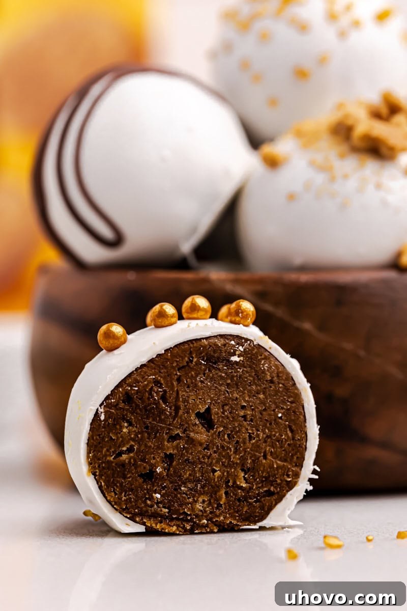A close-up of a gingerbread truffle cut in half, revealing its creamy, spiced interior, placed beside a bowl filled with more whole truffles.