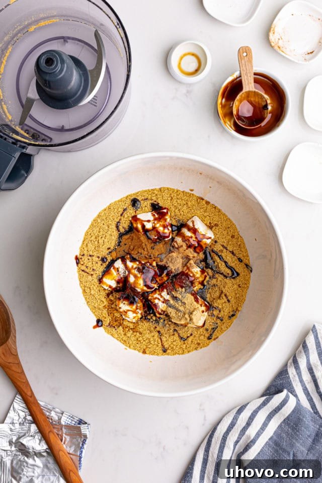 Overhead view of gingersnap cookie crumbs, softened cream cheese, rich molasses, a blend of warm spices, and fragrant vanilla extract in a spacious mixing bowl.