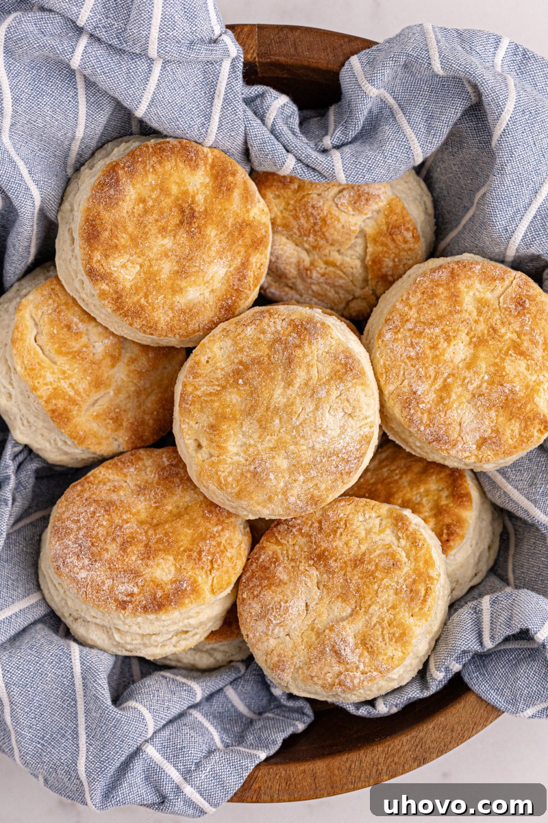 Warm buttermilk biscuits neatly arranged in a wooden bowl lined with a tea towel