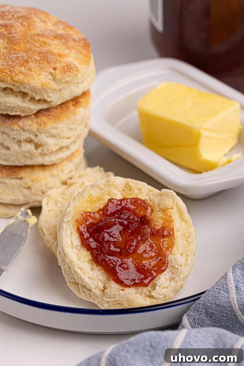 Close-up of a flaky buttermilk biscuit topped with butter and red jam