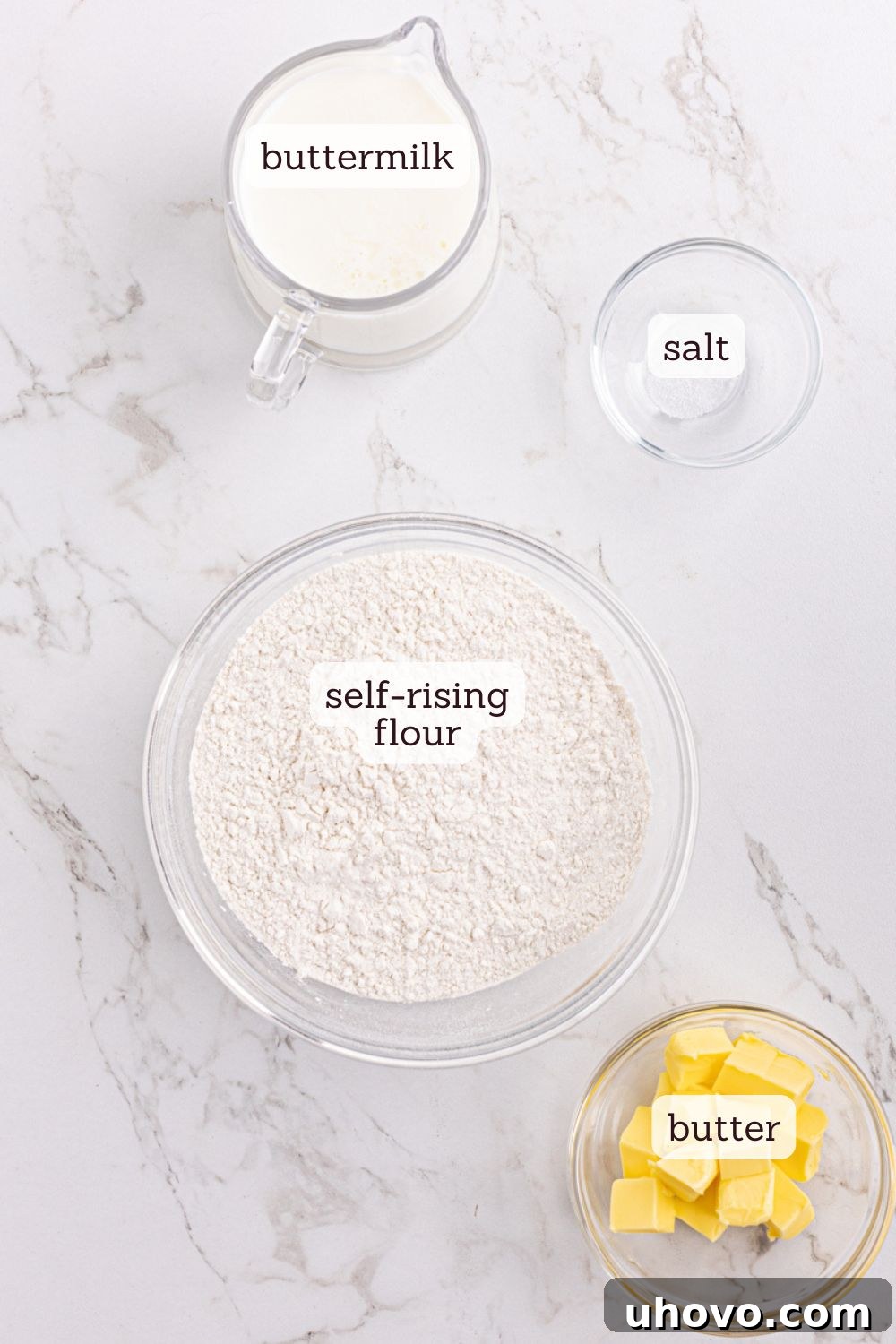 Overhead view of ingredients for buttermilk biscuits with labels: self-rising flour, unsalted butter, buttermilk, salt