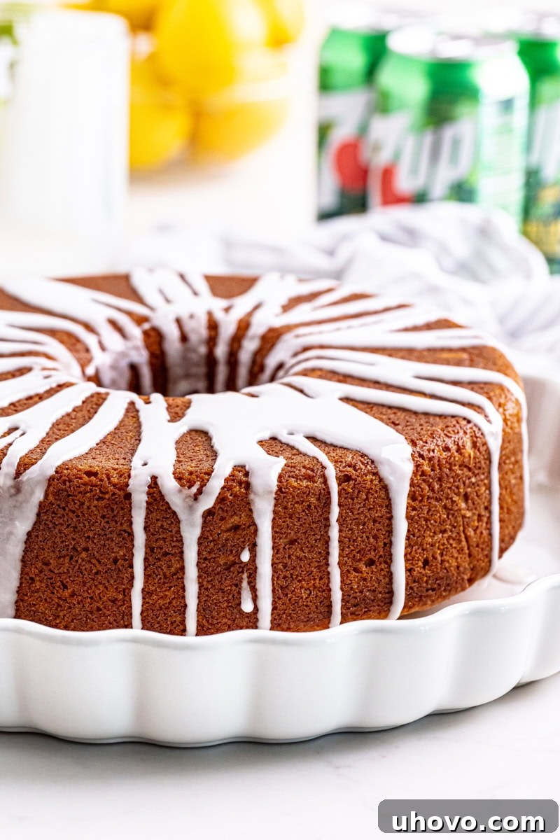 Glazed 7UP cake on a white cake plate with fresh lemons and cans of 7UP in the background, highlighting its refreshing citrus appeal.