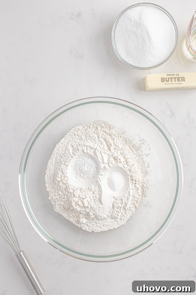 Overhead view of flour, baking powder, and salt measured into a glass mixing bowl, ready to be whisked.