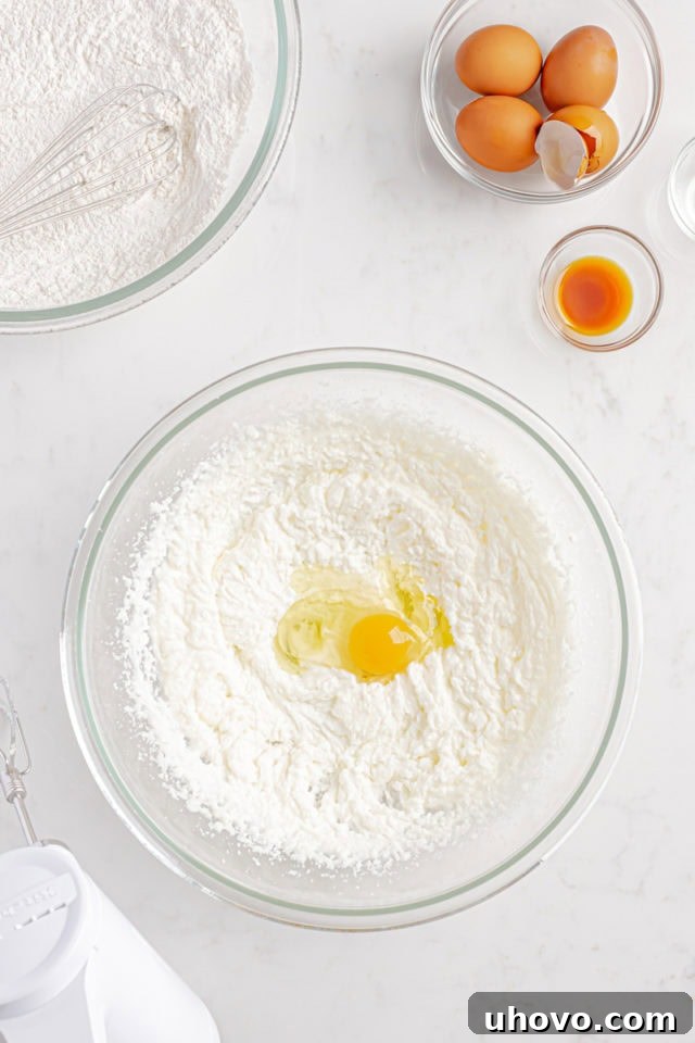 Overhead view of a cracked egg being added to the creamed butter, oil, and sugar mixture in a glass bowl.