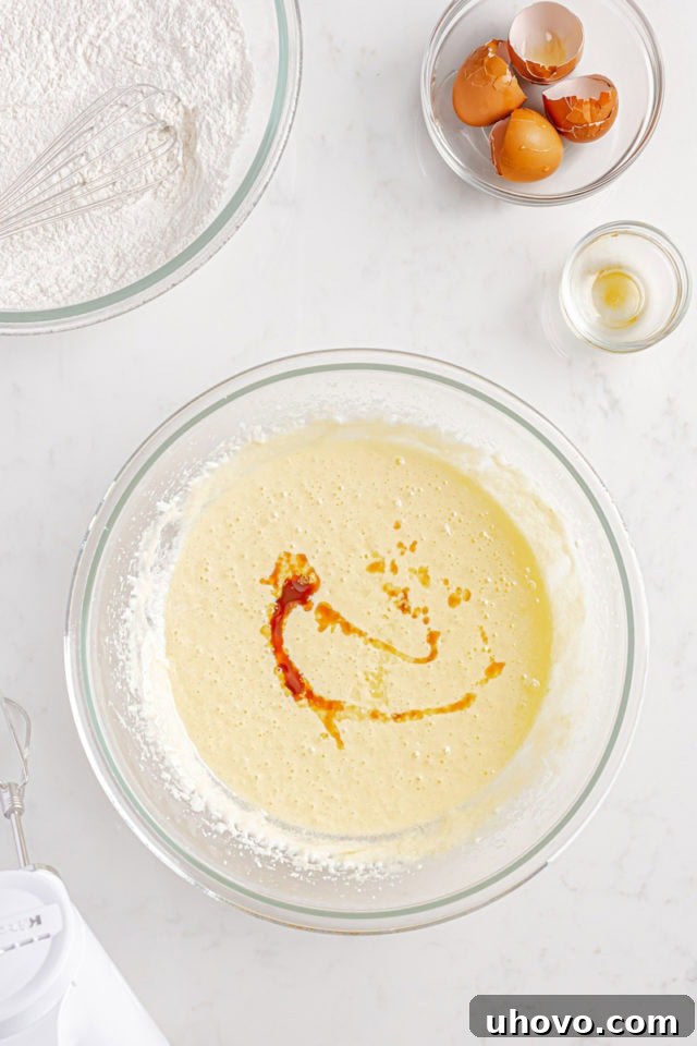 Overhead view of vanilla and lemon extracts being drizzled into the cake batter in a mixing bowl.