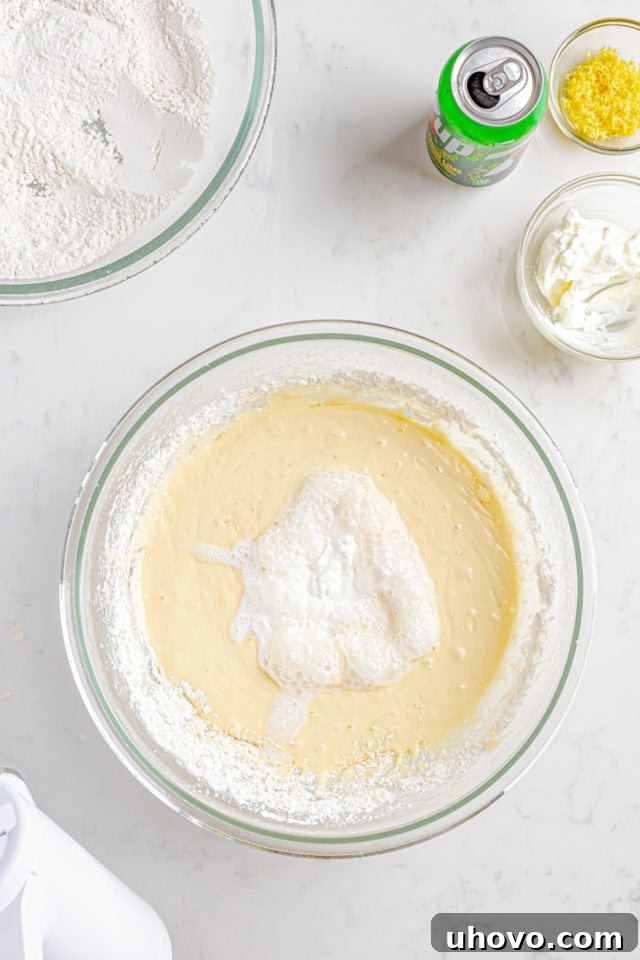 Overhead view of sour cream being added to the cake batter in a mixing bowl, to be alternated with soda.