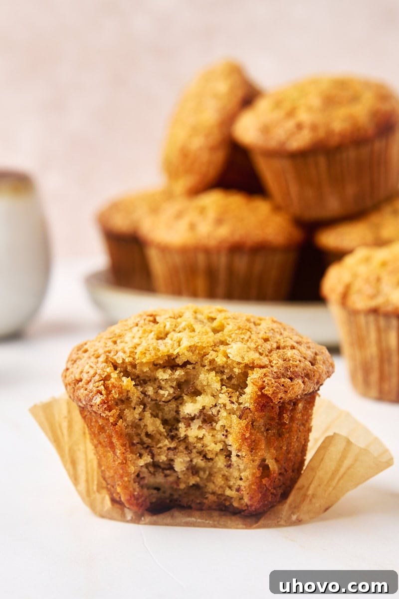 a banana muffin with a bite missing; more muffins on a plate in the background