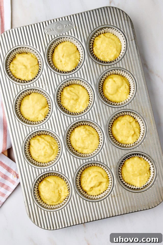 Overhead view of orange ricotta muffin batter neatly portioned into each cup of a 12-cup muffin pan, filling them about three-quarters full