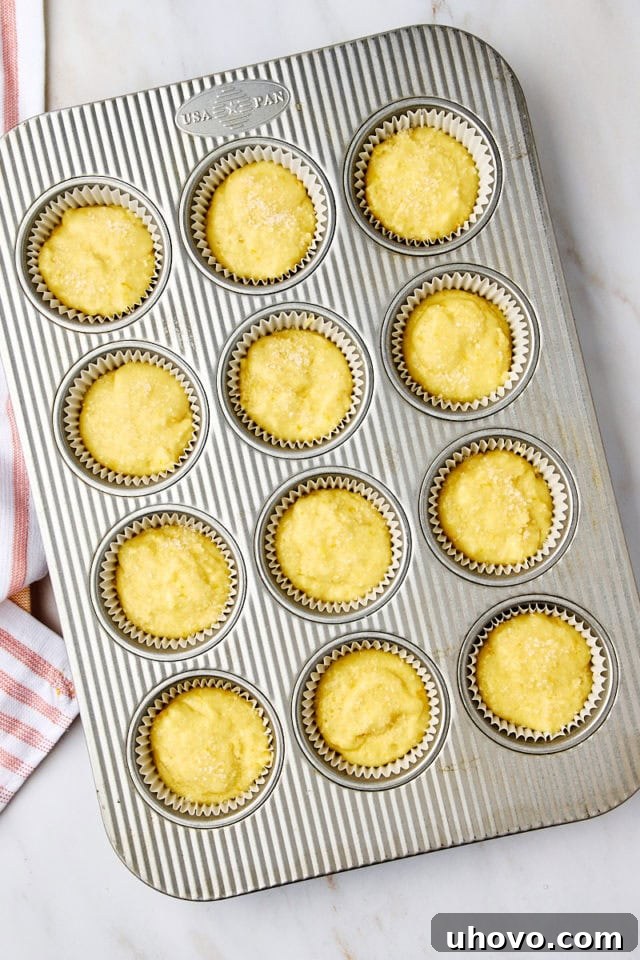 Overhead view of unbaked orange ricotta muffins in a pan, each topped with a sprinkle of coarse sugar, ready to be placed in the oven