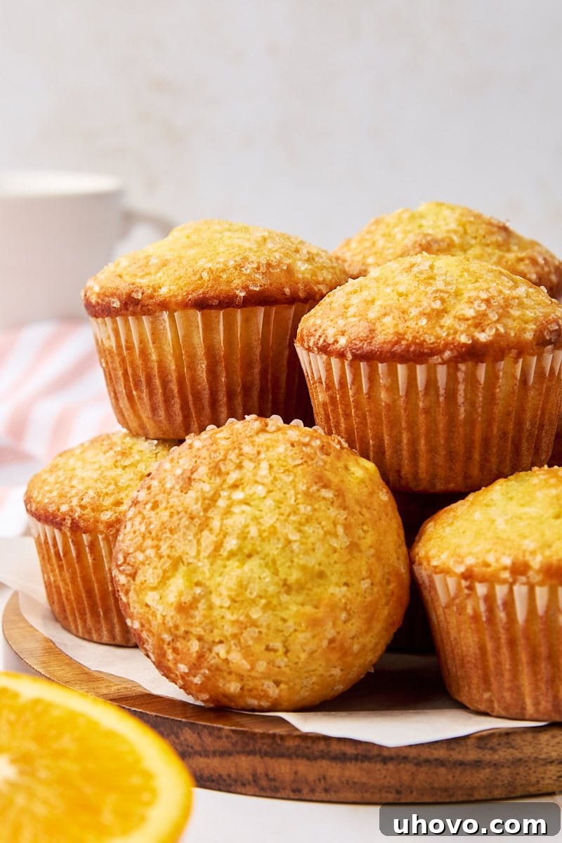 A stack of golden brown orange ricotta muffins on a rustic wooden serving plate, with a few loose crumbs, ready to be enjoyed