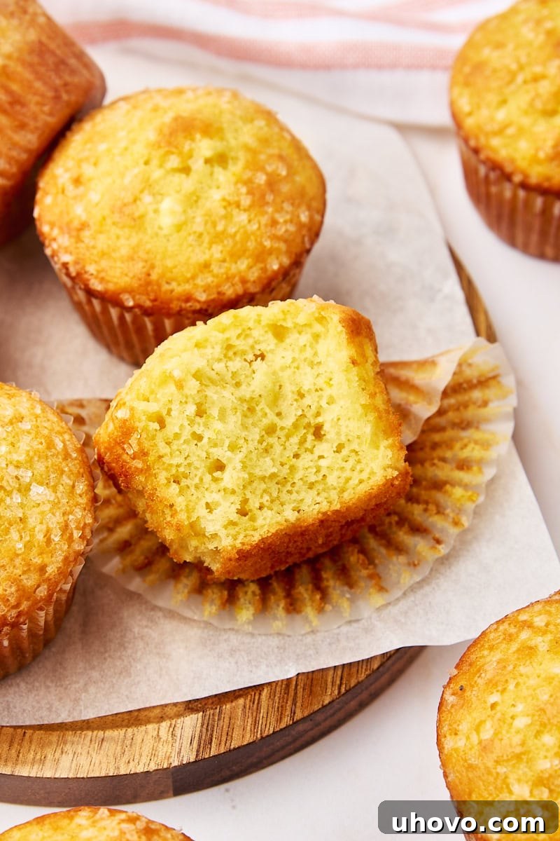 A perfectly halved orange ricotta muffin, revealing its moist, tender crumb with flecks of orange zest, surrounded by other whole muffins