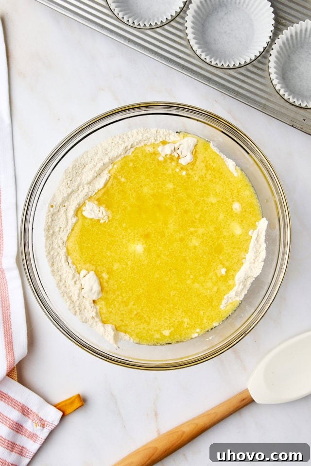 Overhead view of the whisked wet ingredients being poured into the large bowl containing the dry ingredients for orange ricotta muffins