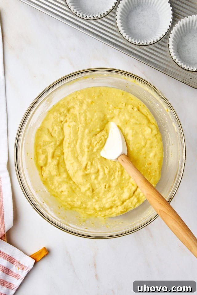 Overhead view of the orange ricotta muffin batter in a glass mixing bowl, showing it just combined with a few streaks of flour remaining