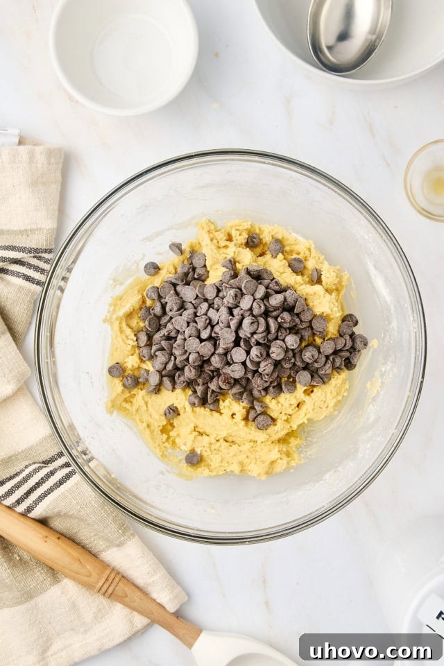 overhead view of chocolate chips added to cookie dough in a glass mixing bowl