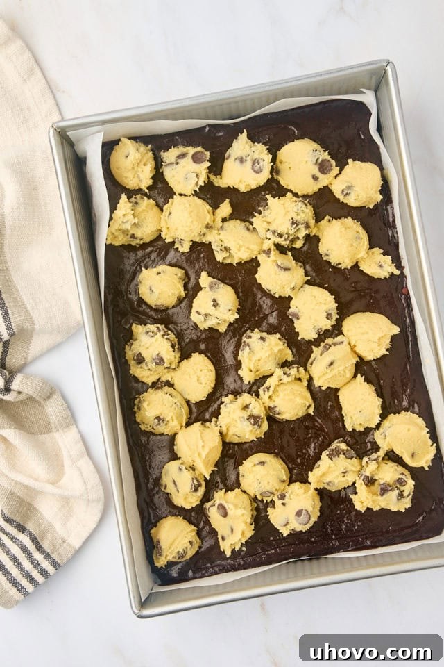 overhead view of chocolate chip cookie dough dropped by spoonfuls onto brownie batter in a 9x13 pan