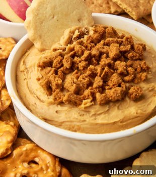 cookie butter dip in a white bowl surrounded by various foods for dipping