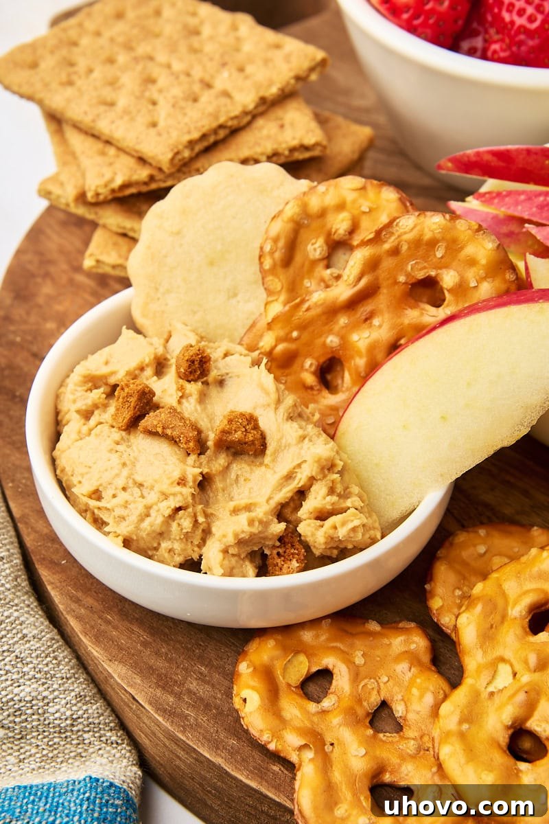 a serving of cookie butter dip in a small bowl with pretzels, shortbread, and an apple slice