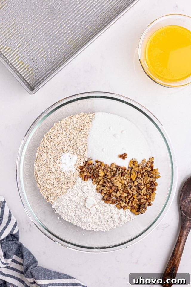 overhead view of flour, oats, sugar, nuts, and baking powder in a glass mixing bowl