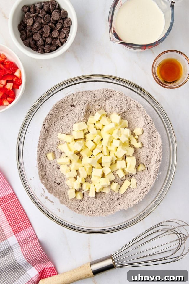 Overhead view of cold, cubed butter being added to the dry ingredients in a mixing bowl.