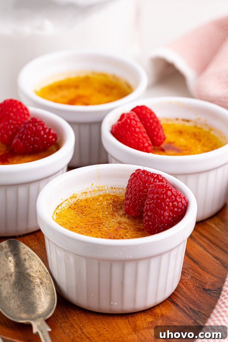 Four ramekins of classic crème brûlée with crisp caramelized sugar toppings arranged elegantly on a rustic wooden serving board, ready to be enjoyed.