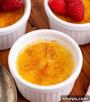 Three ramekins of classic crème brûlée on a rustic wooden serving board, perfectly set and ready to be enjoyed.