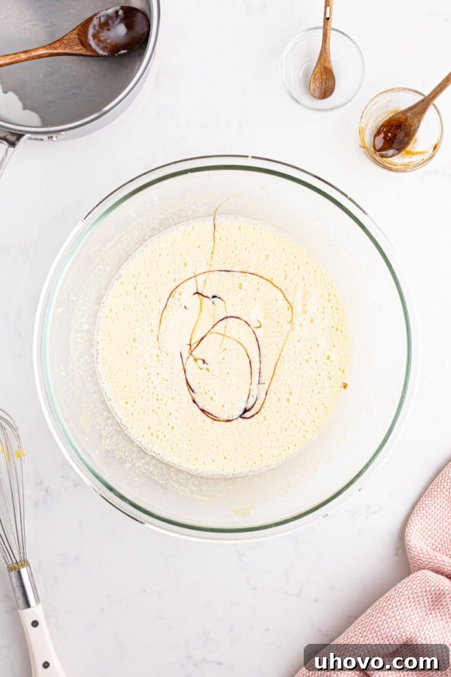 A close-up, overhead view of vanilla bean paste being stirred into the crème brûlée custard mixture in a bowl, showing the characteristic dark flecks.
