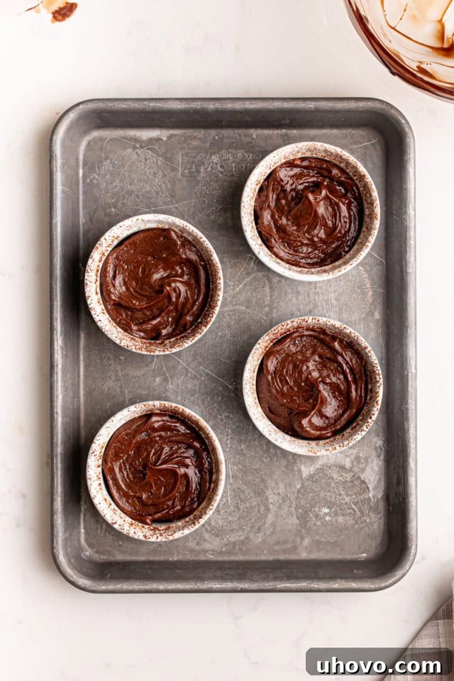 An overhead view of the smooth chocolate lava cake batter perfectly divided among four prepared ramekins, arranged on a baking sheet, ready for the oven.